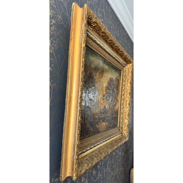 A warm 19th-century pastoral landscape oil painting featuring cattle watering at sunset, rendered in rich earth tones with...