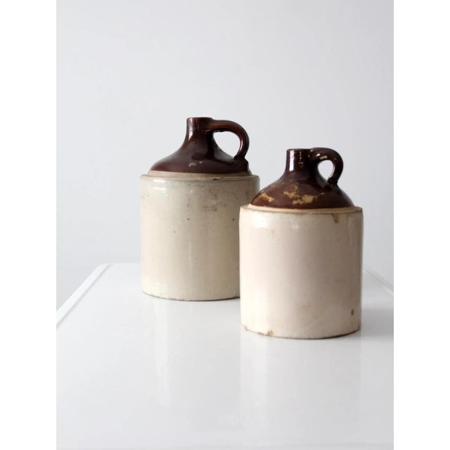 This pair of antique stoneware crock jugs exemplifies classic utilitarian design with rustic charm. Perfect for display on...