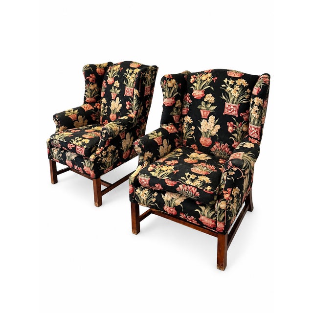 A striking matched pair of wingback armchairs upholstered in a black-ground floral pattern featuring red-and-cream...