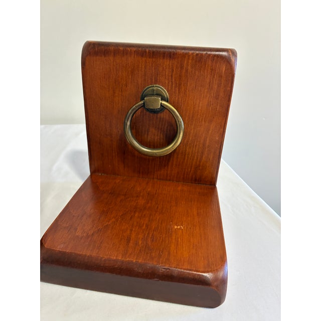 A well-made pair of wood bookends finished in a warm mahogany tone, each fitted with a polished brass ring pull as a...