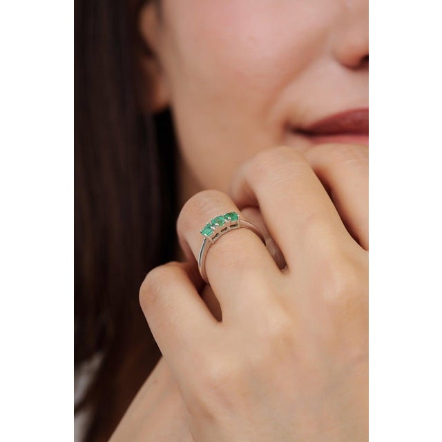 This delicate three-stone emerald ring is crafted in 925 sterling silver and features three vibrant round-cut emeralds...