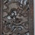 A heavy dark soapstone rectangular panel that is carved with a four- clawed dragon flying in the clouds over sea waves and...