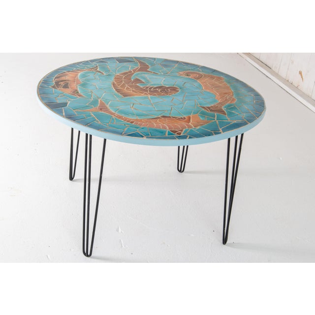 Large round ceramic tile table depicting four large orange fish swimming in blue water.Tile top stands on four black...