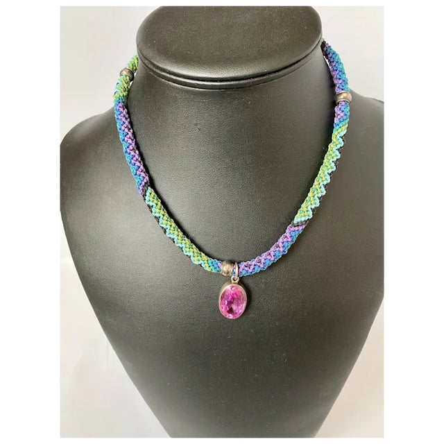 Unique and colorful macrame necklace with oval synthetic pink sapphire pendant. The large vibrant pink stone is set in...