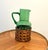 Beautiful vintage green blown glass pitcher featuring a warm woven wicker basket wrap. The rich emerald tone, hand-applied...