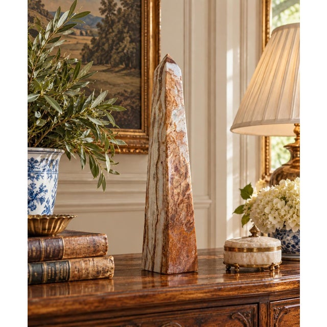 A beautifully proportioned marble obelisk in richly veined shades of brown, green, and cream. The sculptural silhouette...