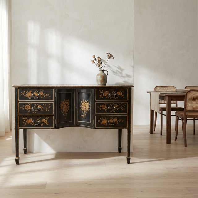 A vintage Chinoiserie-style sideboard featuring a dramatic black lacquered finish with hand-painted gilt floral decoration...