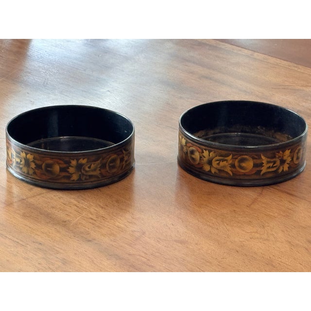 A matched pair of 19th century black papier-mâché wine coasters with dark interiors and gilt-decorated exterior bands....