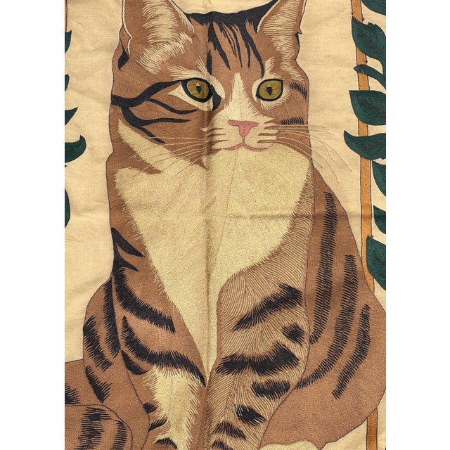 A charming hand embroidered textile wall hanging featuring a beautifully illustrated tabby cat framed by an elegant...