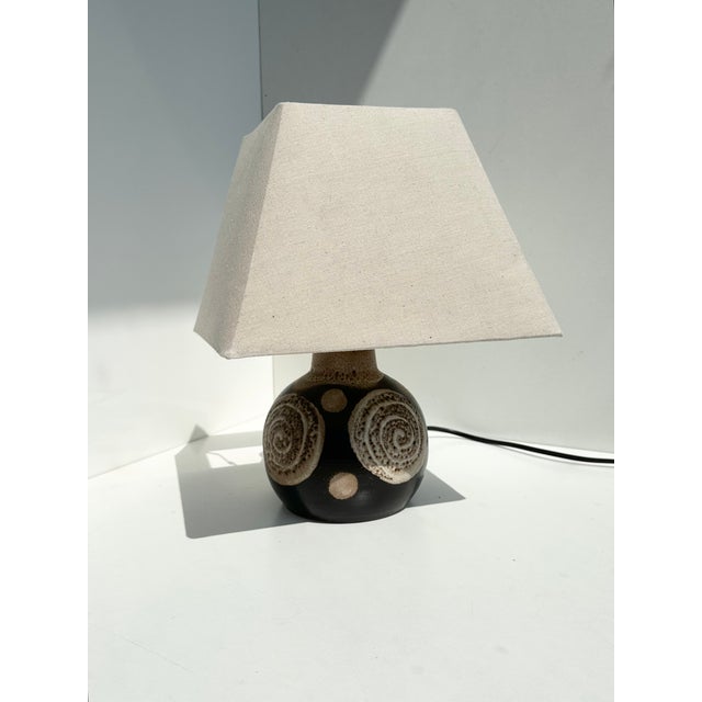 A striking ceramic table lamp with a dark brown glaze and a spiral glaze decoration. The compact, spherical body extends...