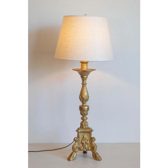 This early 20th-century tripod candlestick, crafted from gilded wood, has been elegantly converted into a lamp while...