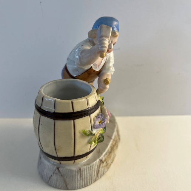 Vintage German match holder and striker of a barrel maker or carpenter with floral accents.