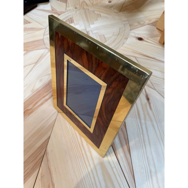 A tabletop picture frame with richly grained wood set inside a wide brass border. A second brass border surrounds the...