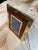 A tabletop picture frame with richly grained wood set inside a wide brass border. A second brass border surrounds the...