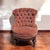 Victorian style tufted slipper chair with pink velvet upholstery and a carved wood base. The chair has a rounded fan-like...