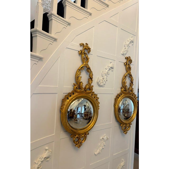 A decorative pair of antique giltwood convex wall mirrors made in the Regency style. Each mirror features an elegant...