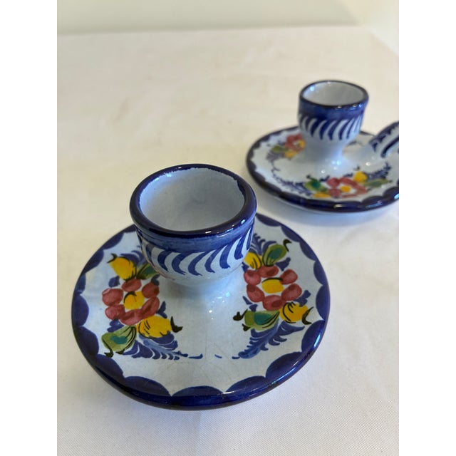 A charming pair of hand painted Portuguese chambersticks with a cobalt blue rim, a scalloped dish, and a cluster of red,...