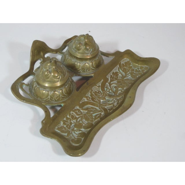 Solid brass Art Nouveau ink stand with two inkwells and pen tray section. It is decorated with intricate raised Nouveau...