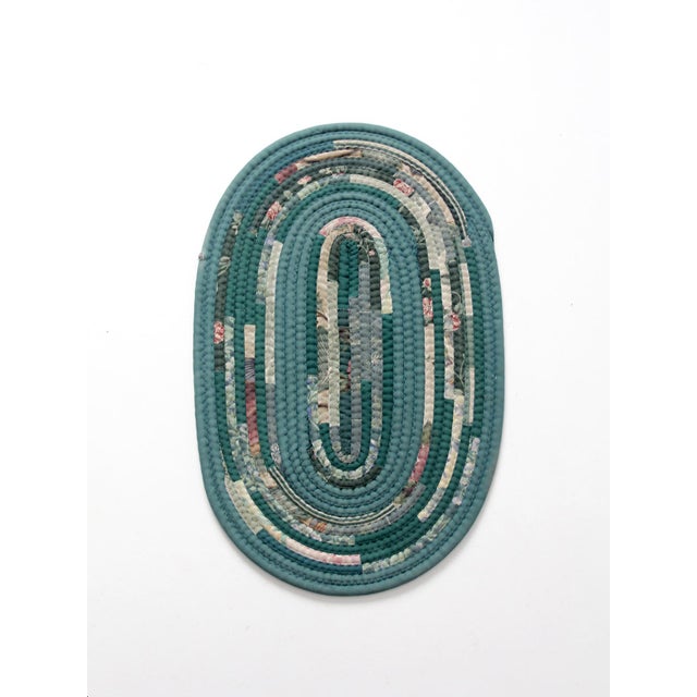 A vintage handmade braided rag rug in a classic oval form, featuring layered green tones with scattered floral accents....