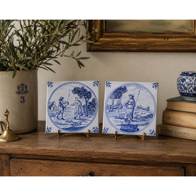 A classic pair of Dutch Delft-style hand painted blue and white Delft ceramic tiles featuring farm landscapes and...