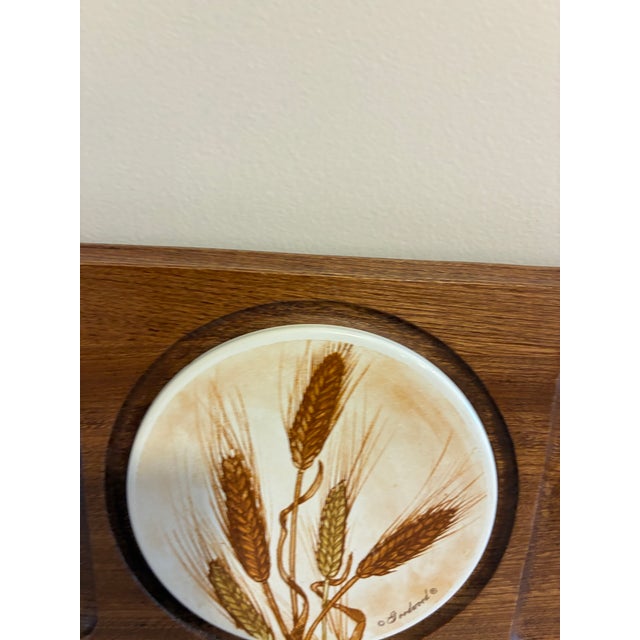 A mid-century teak serving tray by Goodwood, centered with a round ceramic tile trivet printed with a warm-toned wheat...