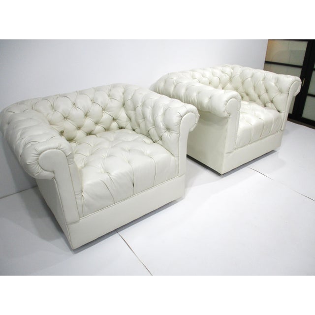 A pair of tufted white leatherette upholstered lounge chairs with rounded arms in the style of a 1970's Chesterfield...