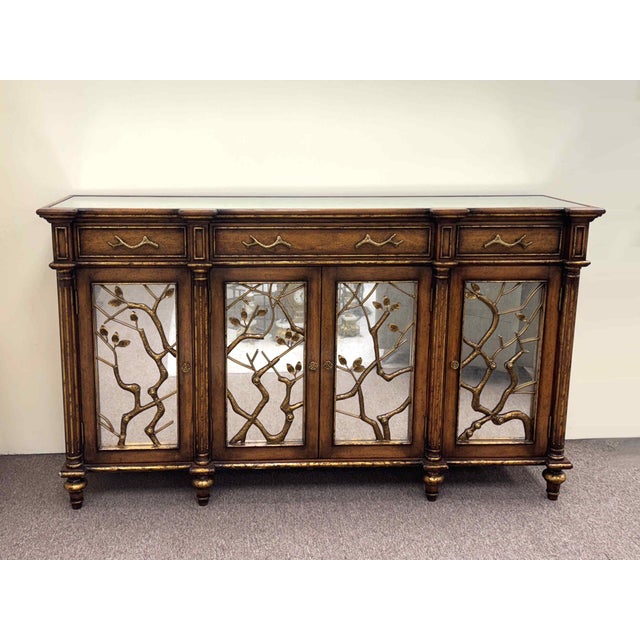 A gorgeous John Richard sideboard featuring richly carved wood details and gilt trim. Four doors are faced with an...