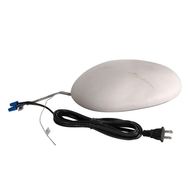 This organic, pebble-shaped wall sconce features a smooth, matte surface adorned with subtle detailing. When illuminated,...