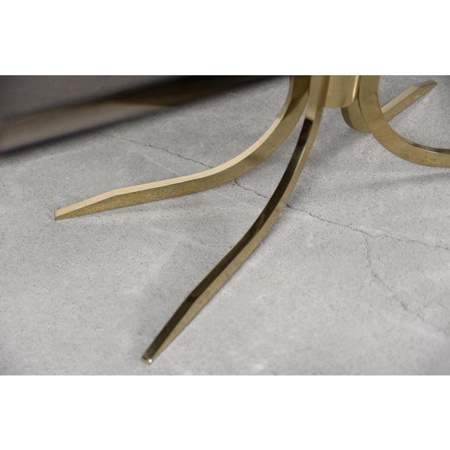 This coffee table was produced during the 1970s. The base is made of four shiny, brass legs that have a raw, sharp form....