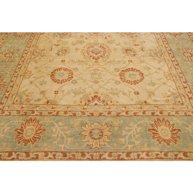 This Modern Turkish wool rug boasts a tan field, beautifully framed with blue, rust, and goldenrod highlights in an...