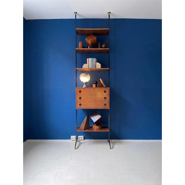 A floor-to-ceiling bookcase from the 1960s, featuring burnished metal uprights and brass end caps. Shaped teak shelves and...