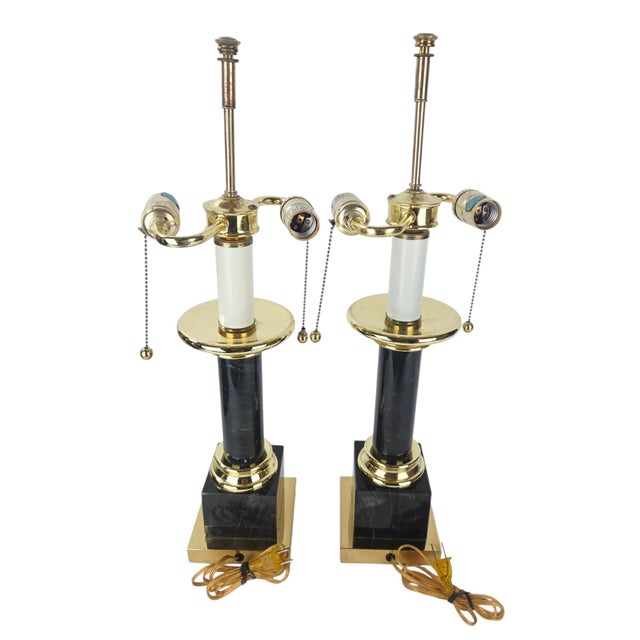 A pair of neoclassical column table lamps in polished brass and black marble, unbranded. Each lamp rises from a stepped...