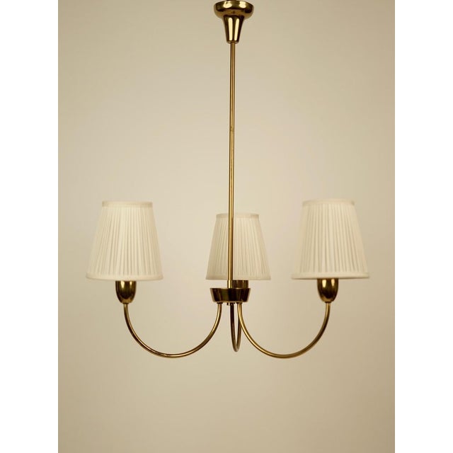 An elegant, brass, three armed pendant from the 1950's, from rupert nikoll. The height of the illustrated lamp is 67 cm....