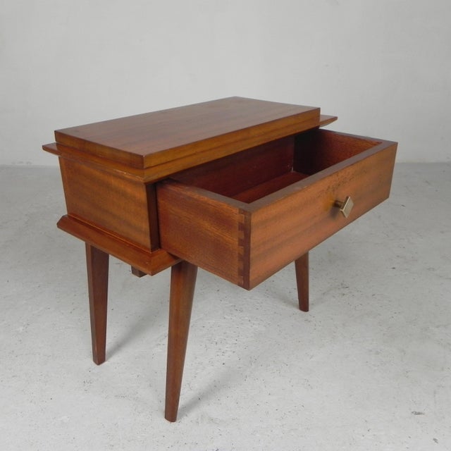 This handy little table also serves as a small cabinet. It features a drawer and angled, tapered legs—typical of mid-...