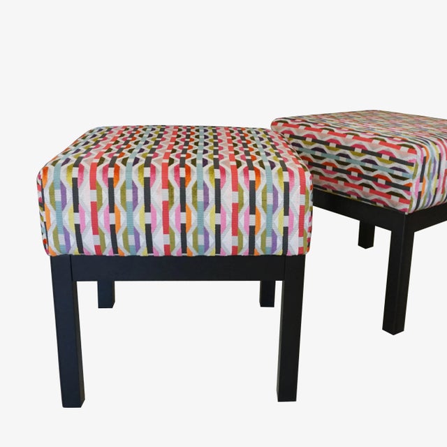 A pair of classic square low stools with cushions upholstered in 'Onetti Chilli' fabric from Romo's Habanera Collection....