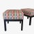 A pair of classic square low stools with cushions upholstered in 'Onetti Chilli' fabric from Romo's Habanera Collection....