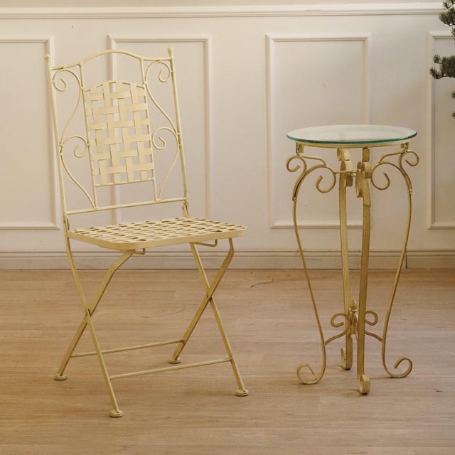 Contemporary side table with a round glass top and an ornately shaped metal frame. The curved lines and slender...