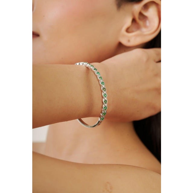 Elegant bangle crafted in 925 sterling silver, featuring approximately 1.6 carats of vibrant green emerald gemstones set...