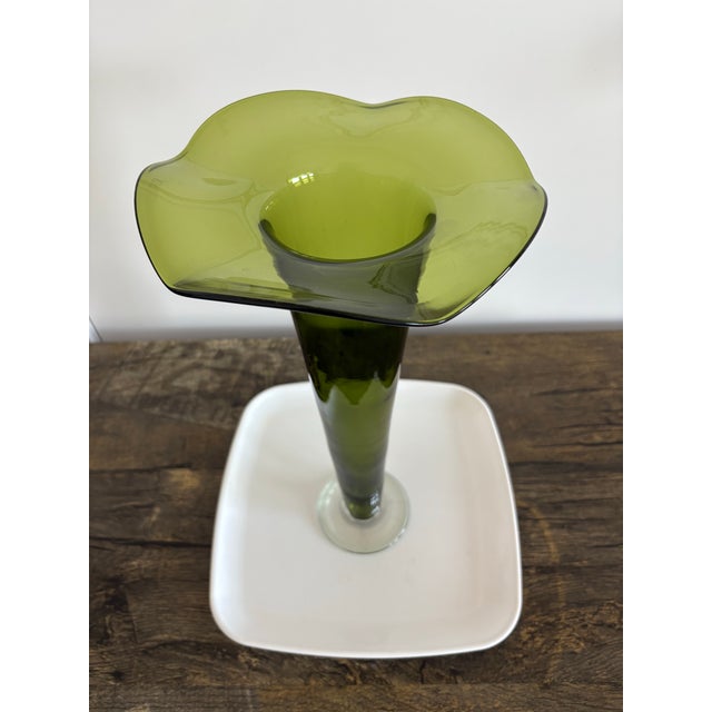 This is a vintage Mid-Century Modern trumpet vase, typically featuring an emerald green glass body with a ruffled rim and...