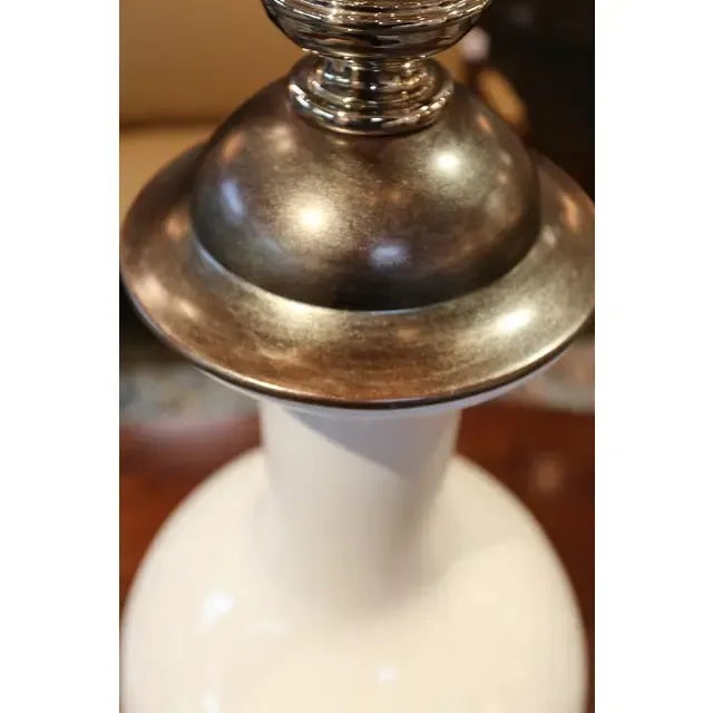 A large ceramic vase in white with stainless steel handles and a silver leaf lid with a bold turned stainless steel finial.