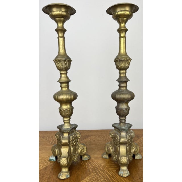 A beautiful pair of vintage brass candle holders featuring elegant turned columns, decorative floral detailing, and ornate...