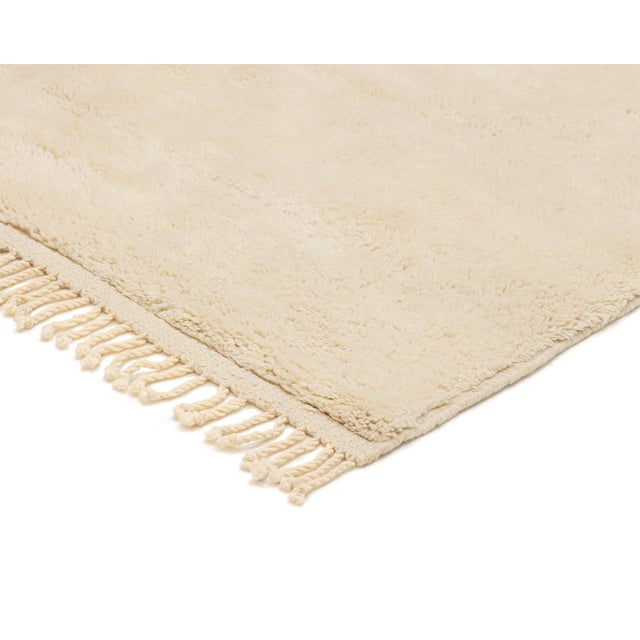 Minimalist hand-knotted wool rug in a rich, Ivory hue, with a plush texture, offering a luxurious underfoot feel and...