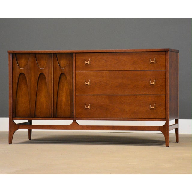 A mid century modern walnut three drawer dresser credenza with swooping walnut and brass arch details made by Broyhill...
