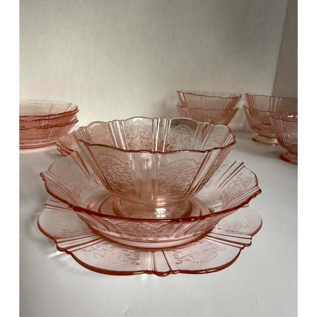 Add a touch of vintage charm to your table with this lovely set of pink Depression-era glass plates and bowls, most likely...