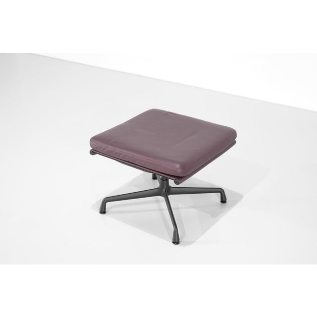 Soft pad chair ottoman stool, model "ea 223 - lounge," in plum-colored leather with red stitching, on a matte black...