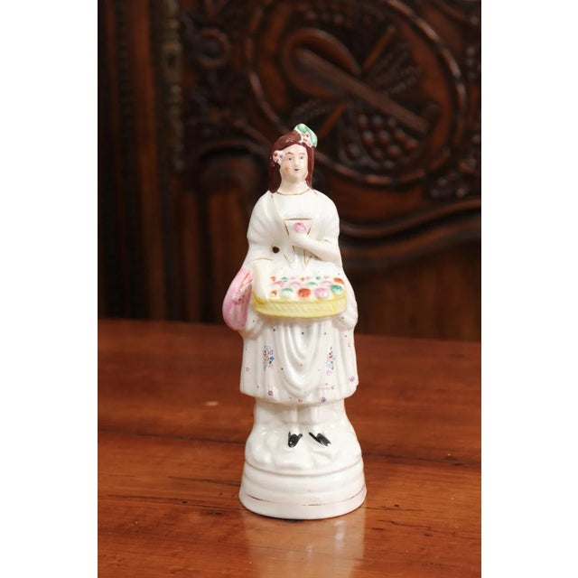 A small English porcelain decorative object depicting a lady carrying a floral basket. Created in England during the 20th...