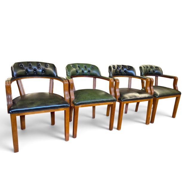 A set of four armchairs in green leather with a curved, button-tufted back and brass nailhead trim. Solid wood frames with...