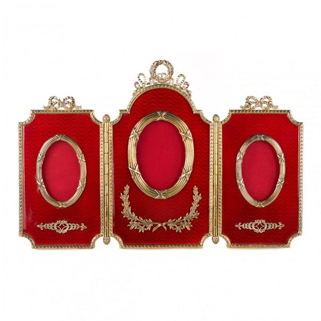 A rare three-part photo frame made of gilt silver, featuring a vivid decorative accent — translucent red enamel over an...