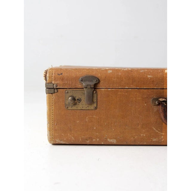 This is a distressed vintage striped suitcase. The hard luggage case features a tan canvas cover with faded yellow...