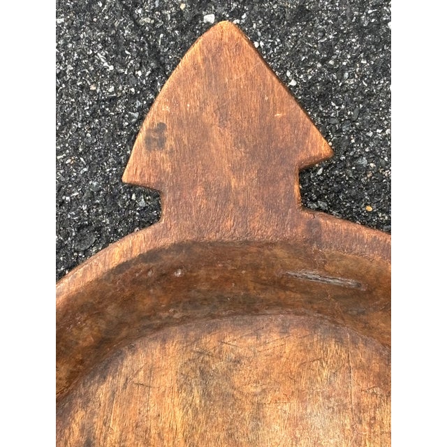 A substantial hand carved wooden bowl with integral arrow-shaped handle, hewn from a single piece of wood. Likely 19th C....